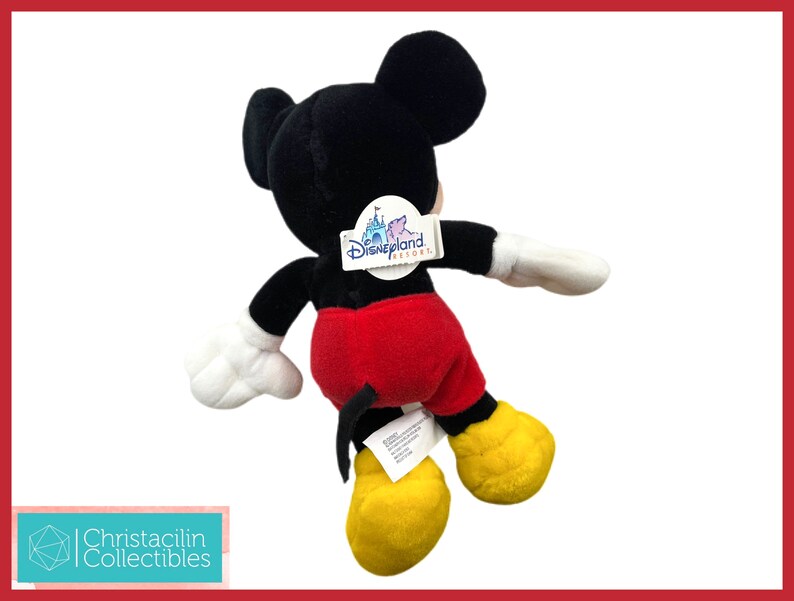 May include: A plush Mickey Mouse toy, viewed from the back, with black fur, red shorts, yellow shoes, and white gloves. The toy has a Disneyland Resort tag attached. The background is white with a red border.