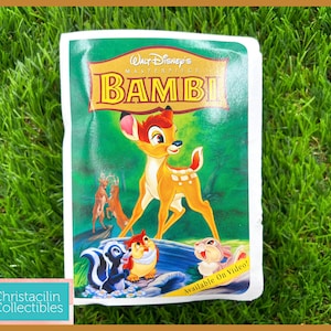 May include: A vintage VHS tape of Disney's animated film "Bambi." The cover features Bambi, Thumper, Flower, and other characters against a green background. The title "Walt Disney's Masterpiece Bambi" is displayed prominently.