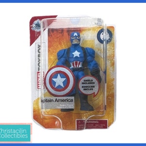 Op de afbeelding: Captain America actiefiguur in originele verpakking. De figuur is blauw met een witte ster op de borst en een bijpassend schild. De verpakking bevat de tekst "Marvel Toybox" en "Shield Included".