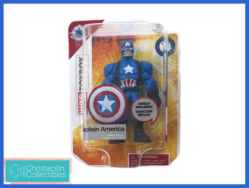 Op de afbeelding: Captain America actiefiguur in originele verpakking. De figuur is blauw met een witte ster op de borst en een bijpassend schild. De verpakking bevat de tekst "Marvel Toybox" en "Shield Included".