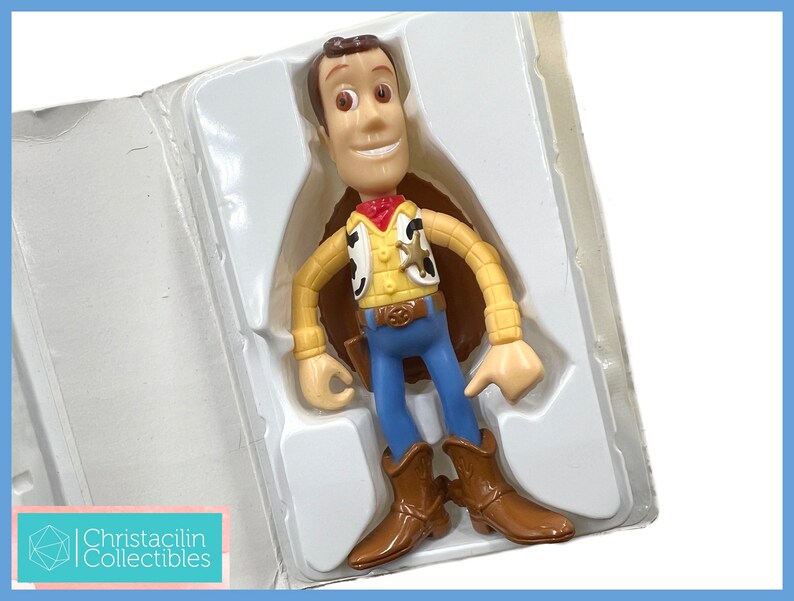 May include: A Woody action figure from the Toy Story franchise, in its original packaging. The figure is wearing a yellow shirt, blue pants, a red bandana, and brown boots. The packaging is white and the figure is in a standing position.