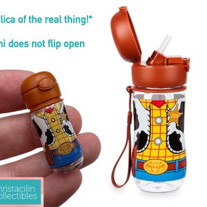May include: A clear plastic water bottle and a miniature replica, both featuring a Woody-themed design. The bottle has a brown lid and a straw. The miniature is held in a hand. The text "Replica of the real thing!" is visible.