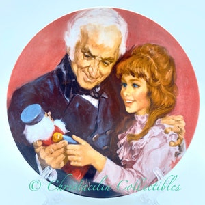 May include: A decorative plate featuring a painting of an older man and a young girl, both smiling. The man, in a dark coat, holds a toy. The girl, with red hair, is embraced by the man. The plate has a red background.