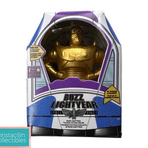 Puede incluir: Figura de acci&oacute;n de Buzz Lightyear dorada en su caja original. La caja presenta un dise&ntilde;o azul, blanco y morado con las palabras "Buzz Lightyear Space Ranger". La figura es visible a trav&eacute;s de una ventana transparente.