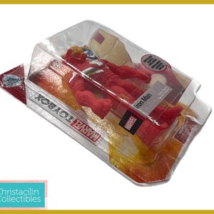 May include: A red Iron Man action figure in a clear plastic package. The figure is in a dynamic pose, with the Marvel logo visible on the packaging. The package is labeled "Iron Man" and "Marvel Toybox".