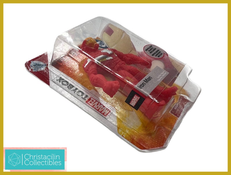 May include: A red Iron Man action figure in a clear plastic package. The figure is in a dynamic pose, with the Marvel logo visible on the packaging. The package is labeled "Iron Man" and "Marvel Toybox".