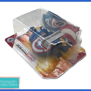 Op de afbeelding: Een Captain America actiefiguur in een doorzichtige plastic verpakking. Het figuur zit met een schild. De verpakking bevat de tekst "Captain America" en "Marvel Toybox". Het schild is rood, wit en blauw.