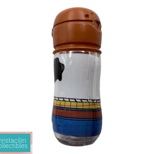 May include: A clear glass salt or pepper shaker with a brown top. The body of the shaker is white with a black cowhide pattern and a blue, yellow, and red design. The shaker is a collectible item.