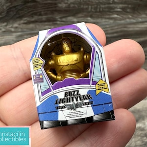 May include: A gold-colored Buzz Lightyear action figure in a box. The box is white, purple, and blue with the words "Buzz Lightyear" and a graphic of a space ship. The box also has text in French.