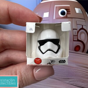 May include: A white Stormtrooper helmet figurine in a small cardboard box. The helmet has black eye coverings and a black mouth piece. The box has the Star Wars logo and the words "First Order Stormtrooper".