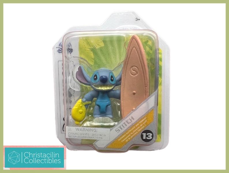 May include: A blue Stitch figurine with a surfboard and a yellow object, packaged in a clear plastic case. The packaging includes the Disney logo and the word "Stitch". The figurine is part of a collectible series.