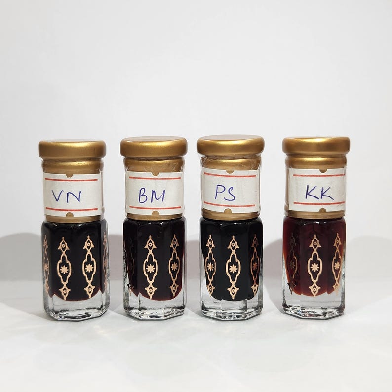 May include: Four small glass bottles with gold lids and labels. The labels have the letters "VN", "BM", "PS", and "KK" written on them. The bottles contain a dark liquid.