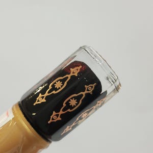 May include: A clear glass bottle with a black and gold design. The bottle is filled with a dark brown liquid.