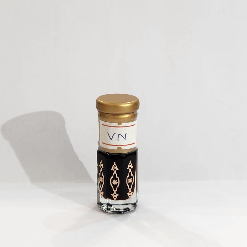 May include: A small glass bottle with a gold lid and a white label that says "VN". The bottle is filled with a dark liquid and has a decorative pattern on the side.