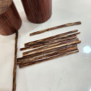 Puede incluir: Primer plano de un montón de virutas de madera marrón y marrón claro. Las virutas están dispuestas en un montón ordenado sobre una superficie blanca.