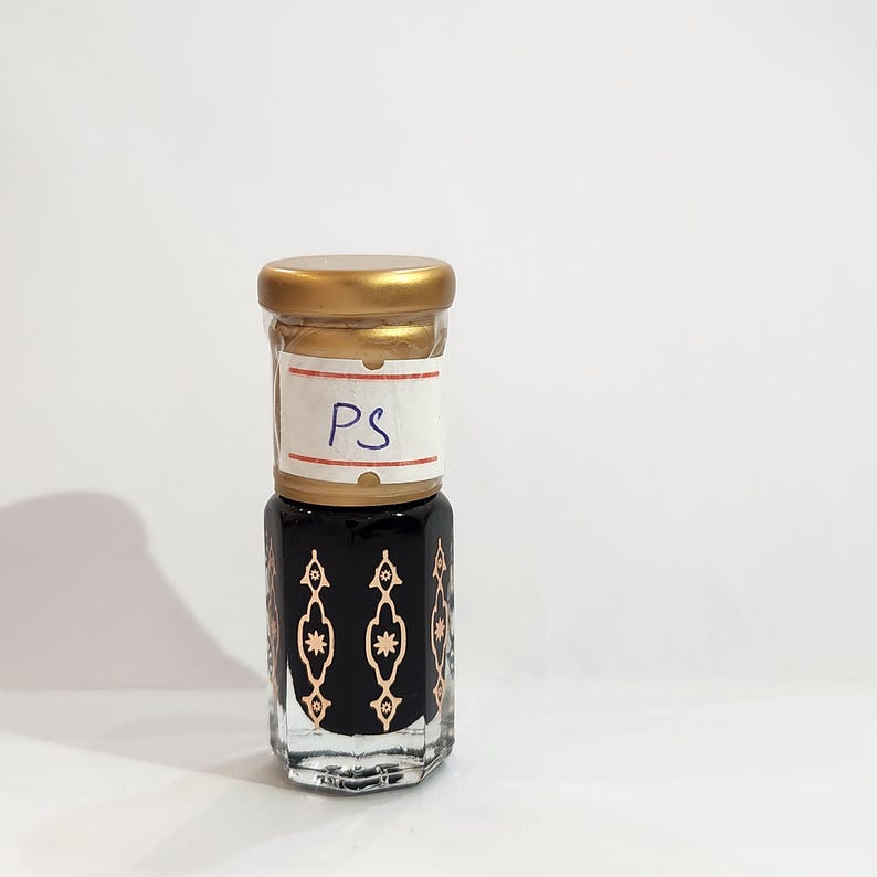 May include: A small glass bottle with a gold lid and a black and gold patterned design. The bottle has a label with the letters "PS" on it.