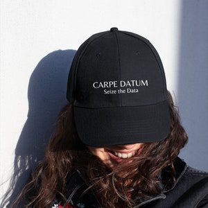 May include: A black baseball cap with white embroidered text that reads "CARPE DATUM Seize the Data".