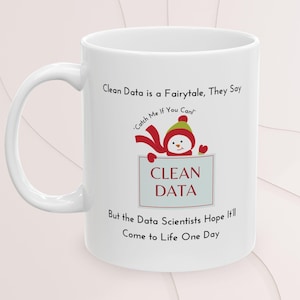 May include: A white ceramic mug with a black handle and the text "But First, Coffee" in a bold, black font. The mug is set against a blurred background, suggesting a cosy setting.