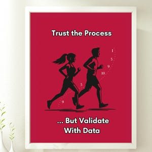 May include: A framed red poster with the text "Trust the Process" at the top and "... But Validate With Data" at the bottom. The poster features black silhouettes of two runners. The poster is displayed on a wooden surface.