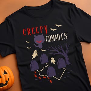 Puede incluir: Camiseta negra con un diseño de Halloween. El diseño incluye un gato sonriente, murciélagos, fantasmas, lápidas y las palabras "Creepy Commits" en rojo y blanco. También se ven calabazas talladas.
