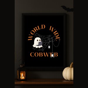 Puede incluir: Un estampado enmarcado con temática de Halloween con fondo negro. El estampado presenta un fantasma usando una computadora portátil, una telaraña y las palabras "WORLD WIDE COBWEB" en naranja. Una silueta de murciélago en la parte superior.