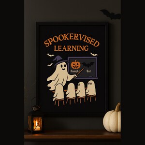 Puede incluir: Un estampado enmarcado con temática de Halloween con las palabras "Spookervised Learning" en naranja. La imagen presenta un fantasma profesor, una calabaza y murciélagos. La impresión está sobre un fondo negro. Una pequeña calabaza y una linterna están en primer plano.