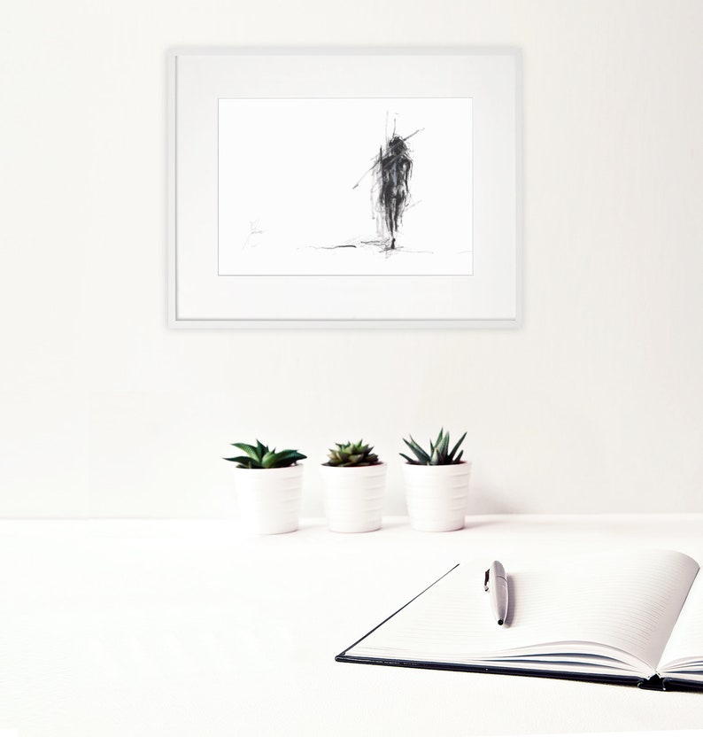 May include: A black and white sketch of a person walking, framed in a white frame and hanging on a white wall. Three small potted plants are on a white surface in front of the frame.