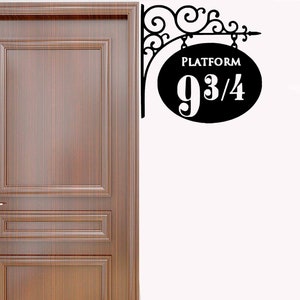 May include: Black metal sign with a decorative scroll design. The sign is shaped like an oval and says "Platform 9 3/4".