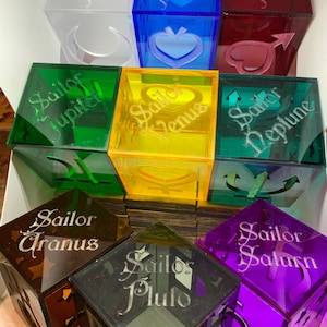 May include: Nine clear acrylic cubes with Sailor Moon characters and their names. Each cube is a different color, including green, blue, red, yellow, brown, gray, and purple. The cubes are stacked in a pyramid shape.