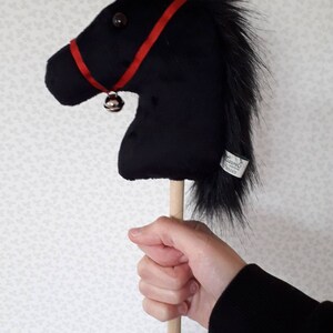 May include: A black plush horse head on a wooden stick with a red ribbon and a bell.