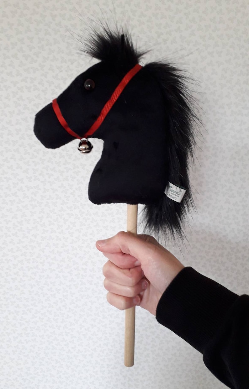 May include: A black plush horse head on a wooden stick with a red ribbon and a bell.