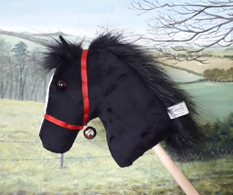 May include: Black plush rocking horse with a red bridle and a bell. The horse has a long black mane and tail. The horse is on a wooden stick. The horse has a label that says "Laurels of the Ponies".
