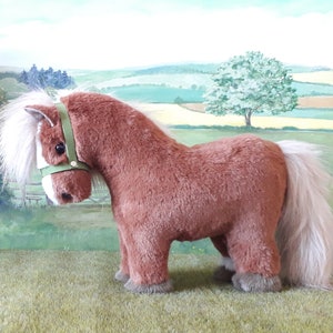 Puede incluir: Un caballo de peluche marr&oacute;n con una crin y una cola blancas. El caballo lleva una cabezada verde.