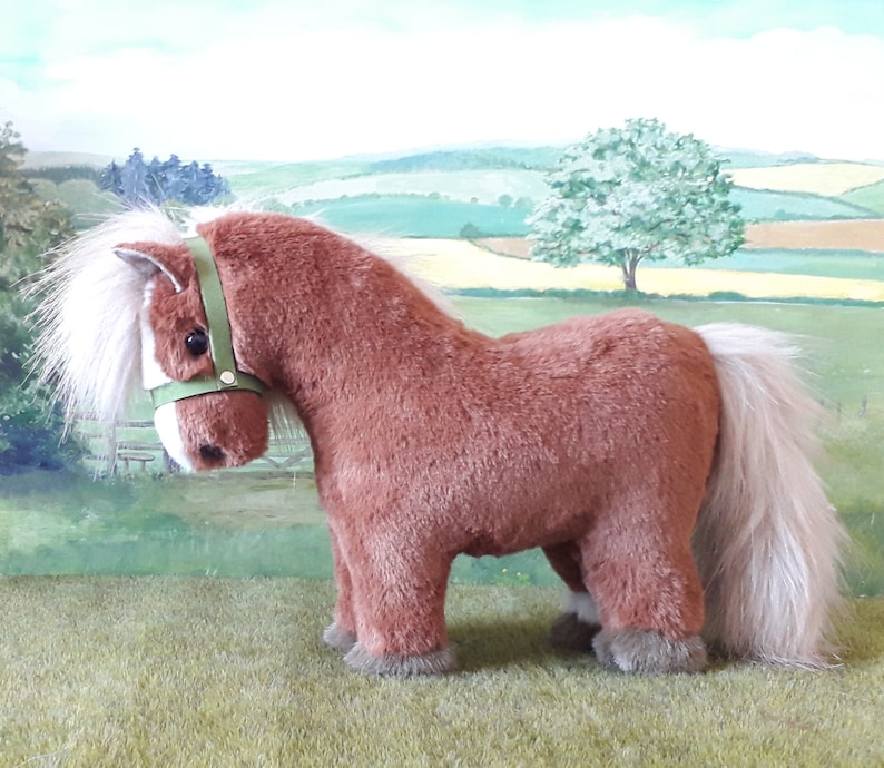 Puede incluir: Un caballo de peluche marr&oacute;n con una crin y una cola blancas. El caballo lleva una cabezada verde.