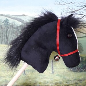 May include: Black plush horse head with a red bridle and a silver bell. The horse head is attached to a wooden stick.