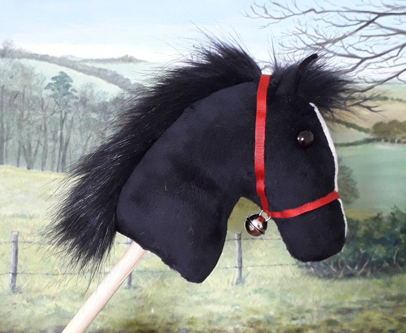 May include: Black plush horse head with a red bridle and a silver bell. The horse head is attached to a wooden stick.