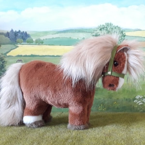 Puede incluir: Un pony de peluche marr&oacute;n con la cara blanca y las pezu&ntilde;as blancas. El pony tiene una melena y una cola largas y fluidas. Lleva una cabezada verde.