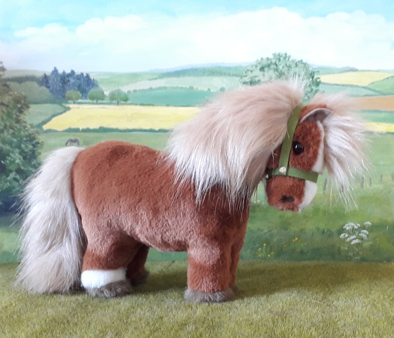 Puede incluir: Un pony de peluche marr&oacute;n con la cara blanca y las pezu&ntilde;as blancas. El pony tiene una melena y una cola largas y fluidas. Lleva una cabezada verde.