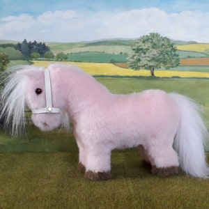 K&ouml;nnte beinhalten: Ein rosa Pl&uuml;schpony mit wei&szlig;er M&auml;hne und Schweif. Das Pony tr&auml;gt ein wei&szlig;es Lederhalfter.