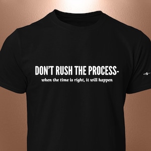 Op de afbeelding: Zwart T-shirt met ronde hals en de witte tekst "DON'T RUSH THE PROCESS - when the time is right, it will happen". Er staat een klein ontwerp op de rechter mouw. Dit T-shirt is een casual kledingstuk.