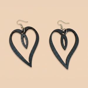 May include: A pair of dark gray heart-shaped earrings. Each earring features a large heart outline with a smaller, elongated heart shape inside. The earrings hang from silver-colored fish hook ear wires.