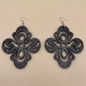May include: A pair of black wooden earrings. Each earring features a symmetrical, openwork design with a floral or quatrefoil shape. The earrings have silver-colored fish hook ear wires.