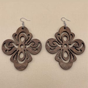 May include: A pair of wooden earrings with a dark brown finish. Each earring features a four-leaf clover design with intricate cut-out patterns and silver-colored ear wires. The earrings are displayed on a neutral background.