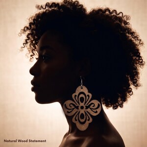 May include: Silhouette of a person with curly hair wearing large, light-colored wooden earrings. The earrings have a decorative, openwork design. The text "Natural Wood Statement" is at the bottom of the image.