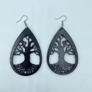 May include: A pair of black teardrop-shaped earrings. Each earring features a cut-out design of a tree with roots and branches. The earrings have silver-colored fish hook ear wires.