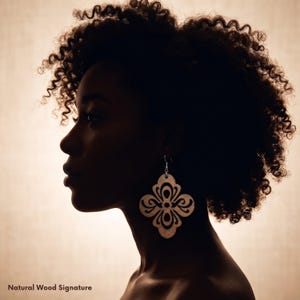 May include: Silhouette of a person with curly hair wearing a pair of wooden earrings. The earrings are a light brown color and feature a floral design. The text "Natural Wood Signature" is at the bottom of the image.