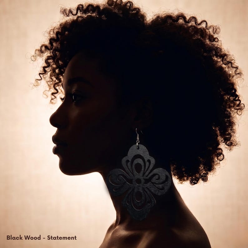May include: Silhouette of a person with curly hair wearing large, black wooden statement earrings. The earrings have a floral design. The text "Black Wood - Statement" is at the bottom of the image.