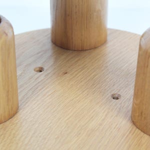 May include: Close-up of a wooden light fixture base with three cylindrical bulb holders. The base is a light-colored wood, and the holders are made of the same material. The fixture is designed to hold light bulbs.