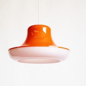 May include: A retro-style pendant light fixture with a vibrant orange top and a white, saucer-shaped bottom. The light hangs from a single cord against a plain white background. The fixture's design is reminiscent of mid-century modern aesthetics.