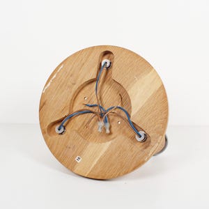 May include: A round, wooden light fixture base with visible wood grain. The base has three holes with wires and a central recessed area. Blue and brown wires are visible. The fixture is set against a white background.
